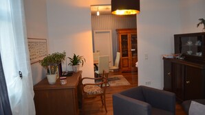 Una sala de estar con una mesa de comedor de madera, dos sillas, un sofá, un armario y una lámpara colgante.