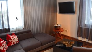 Una sala moderna con un sofá gris, almohadas rojas, un televisor de pantalla plana, una pequeña mesa de madera con un tazón y una mesa de centro de vidrio.