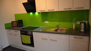 Una cocina moderna con armarios blancos, un salpicadero verde, un lavamanos de acero inoxidable y un horno empotrado.