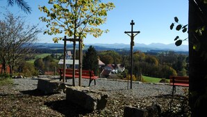 A park with benches, a cross, and a view of houses and mountains.