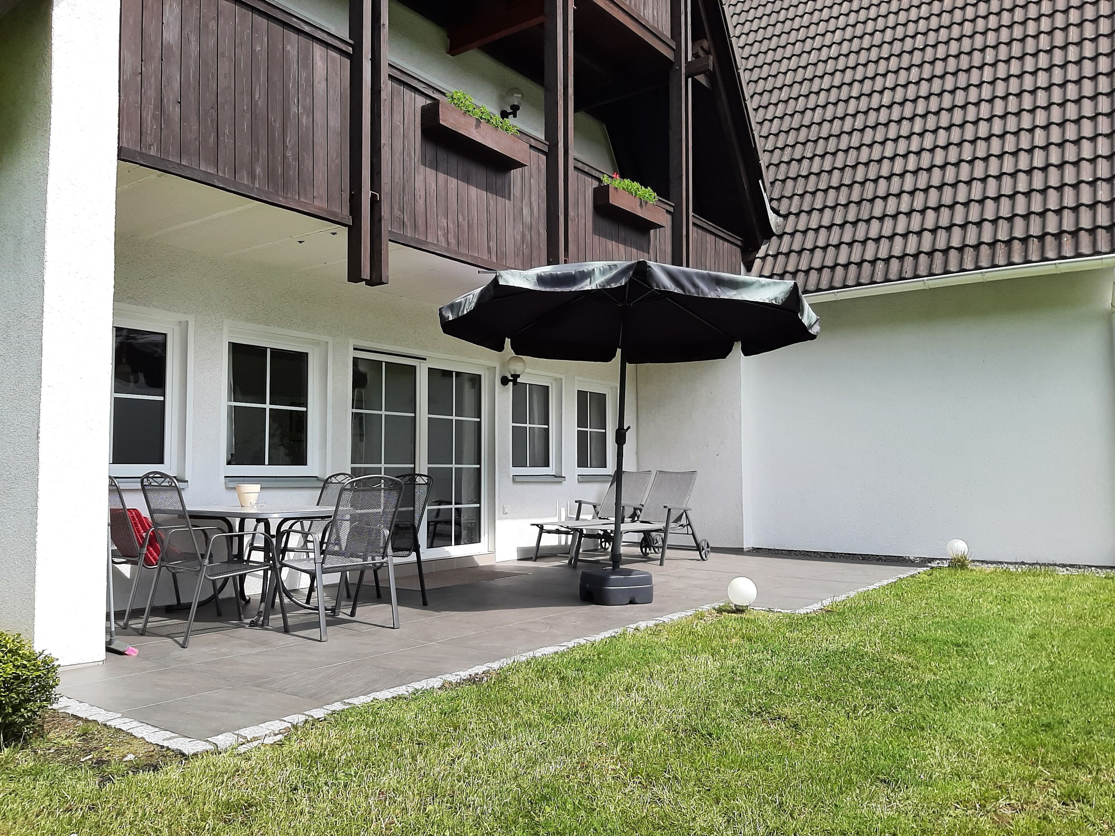 Un patio con mobiliario exterior, una sombrilla y un pequeño césped.
