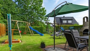 A backyard with a swing set, slide, patio furniture, and a barbecue grill. - The child-friendly holiday house starfish ín Zierow at Wismar (Zierow)