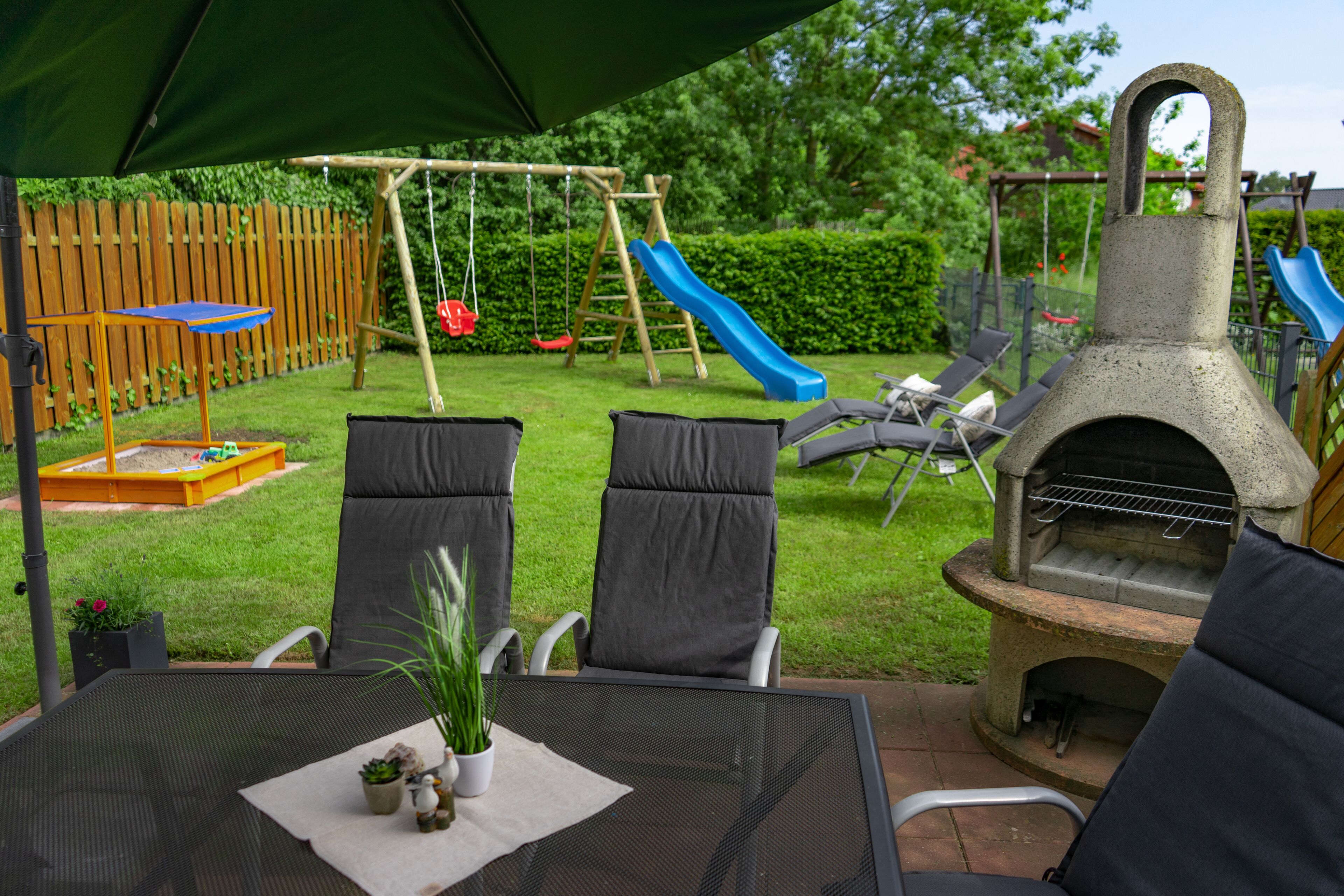 An outdoor patio with a table, chairs, a grill, and a children's play area with a slide.