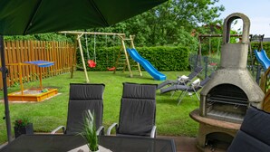 An outdoor patio with a table, chairs, a grill, and a children's play area with a slide. - The child-friendly holiday house starfish ín Zierow at Wismar (Zierow)