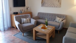 A living room with two grey sofas, a wooden coffee table, and a flat-screen TV mounted on the wall. - The child-friendly holiday house starfish ín Zierow at Wismar (Zierow)