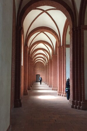 Un pasillo con columnas de ladrillo en arco y una persona caminando hacia una puerta.
