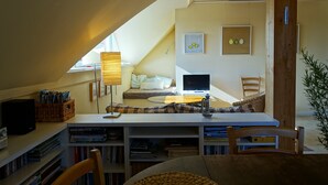 Un dormitorio acogedor en el ático con una cama de altillo, un escritorio con una computadora y una estantería llena de libros.