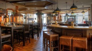 Een restaurantinterieur met een bar, houten tafels en hangende lampen.