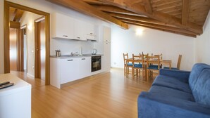 A modern kitchen with white cabinets and a wooden ceiling, a dining area with a blue sofa and wooden chairs, and a small table with a remote control. - 3-room apartment to 6 persons with balcony  (Domaso)