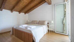 A bedroom with a wooden ceiling, a bed with a white bedspread, a bedside table with a lamp, and a sliding glass door to the right. - 3-room apartment to 6 persons with balcony  (Domaso)