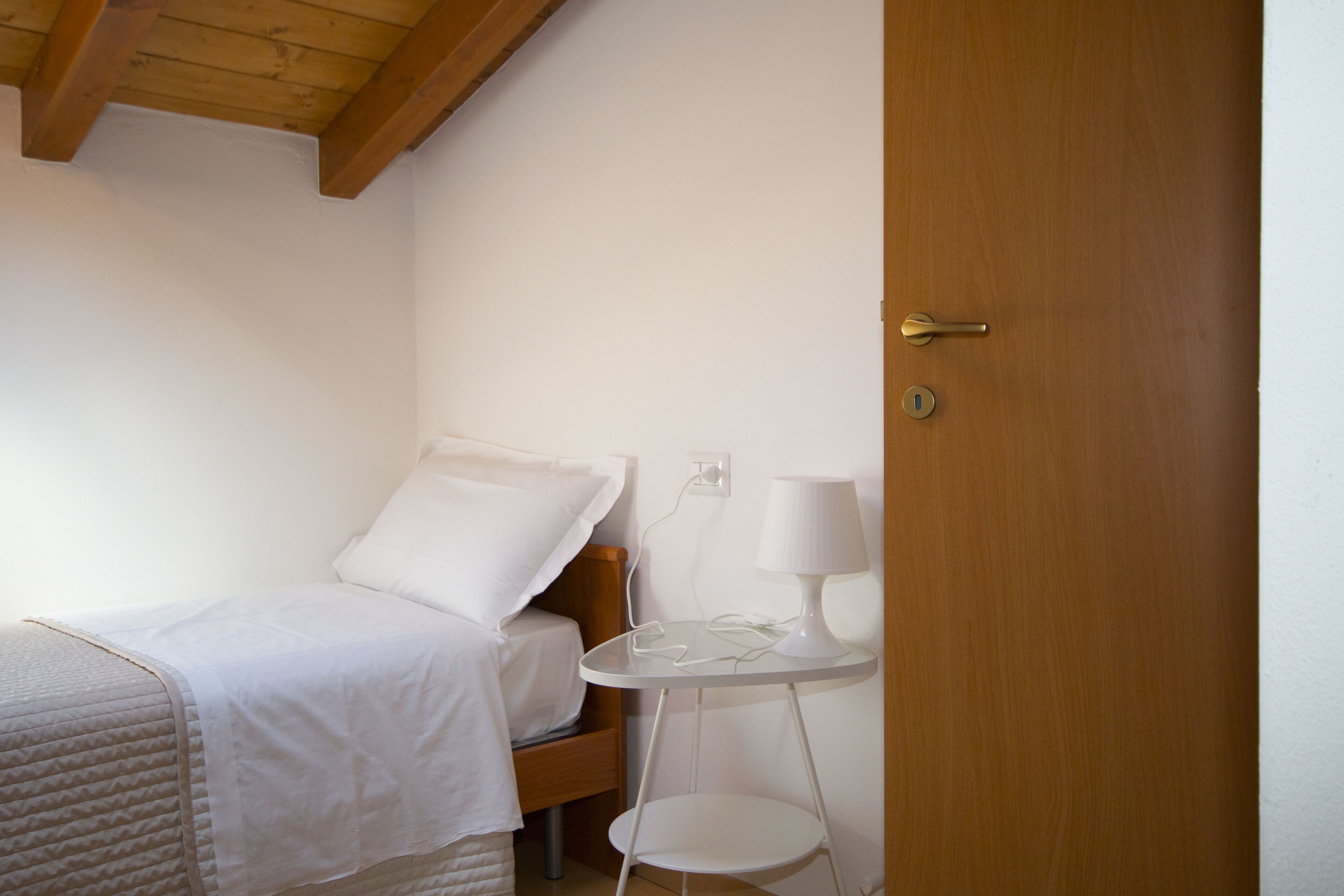 Un dormitorio pequeño y ordenado con cama, mesita de noche, lámpara y una puerta.