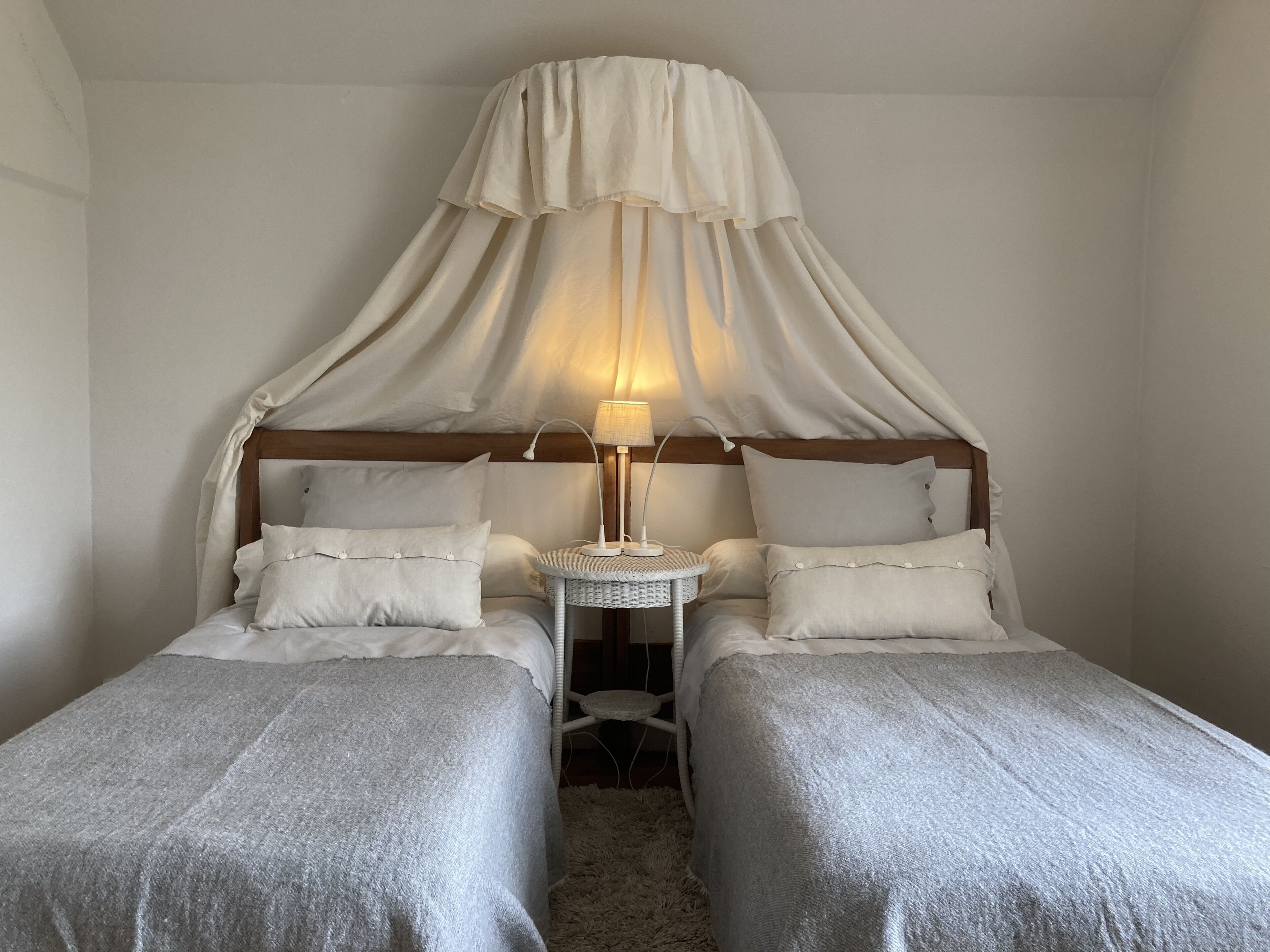 A room with two single beds, a small round table with a lamp, and a canopy over the beds.