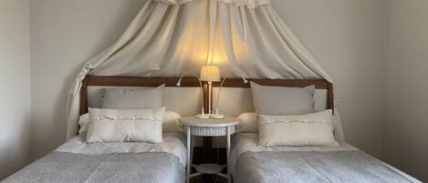 A room with two single beds, a small round table with a lamp, and a canopy over the beds.