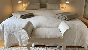 Ein ordentlich gemachtes Bett mit Kissen, einer zusammengeklappten Decke und einem Stuhl in einem Raum mit zwei Wandlampen.