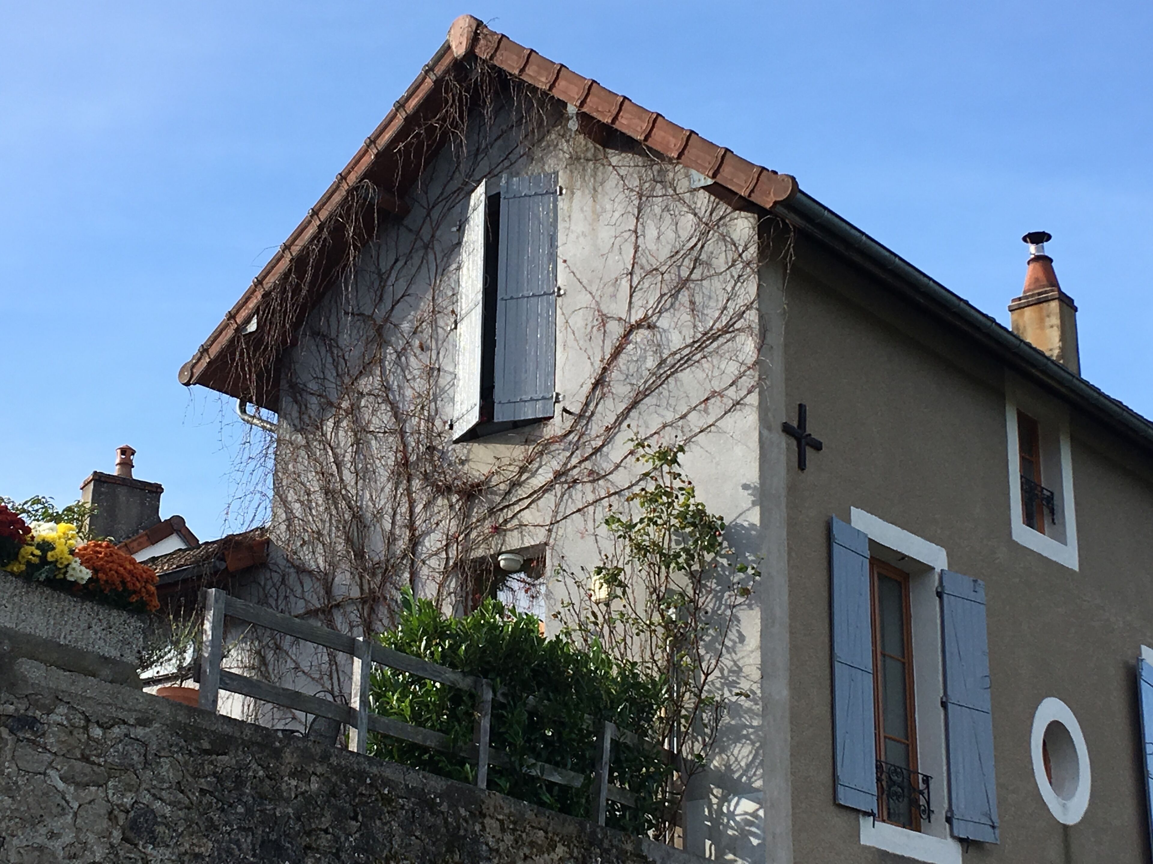 Une maison à deux étages avec un mur en pierre, une clôture en bois et un jardin fleuri.