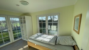 A bedroom with a bed, a wardrobe, and a large window with a view of a garden. - LandHausFewo 9a for 5 friends with baby / dog in a secluded rural location (Greven)