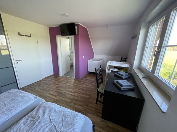 Een knus kamertje met een bed, een bureau en een stoel, een raam met uitzicht en een deur naar een badkamer.