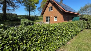 A brick house with a sloped roof and solar panels, surrounded by well-maintained hedges and trees. - LandHausFewo 9a for 5 friends with baby / dog in a secluded rural location (Greven)