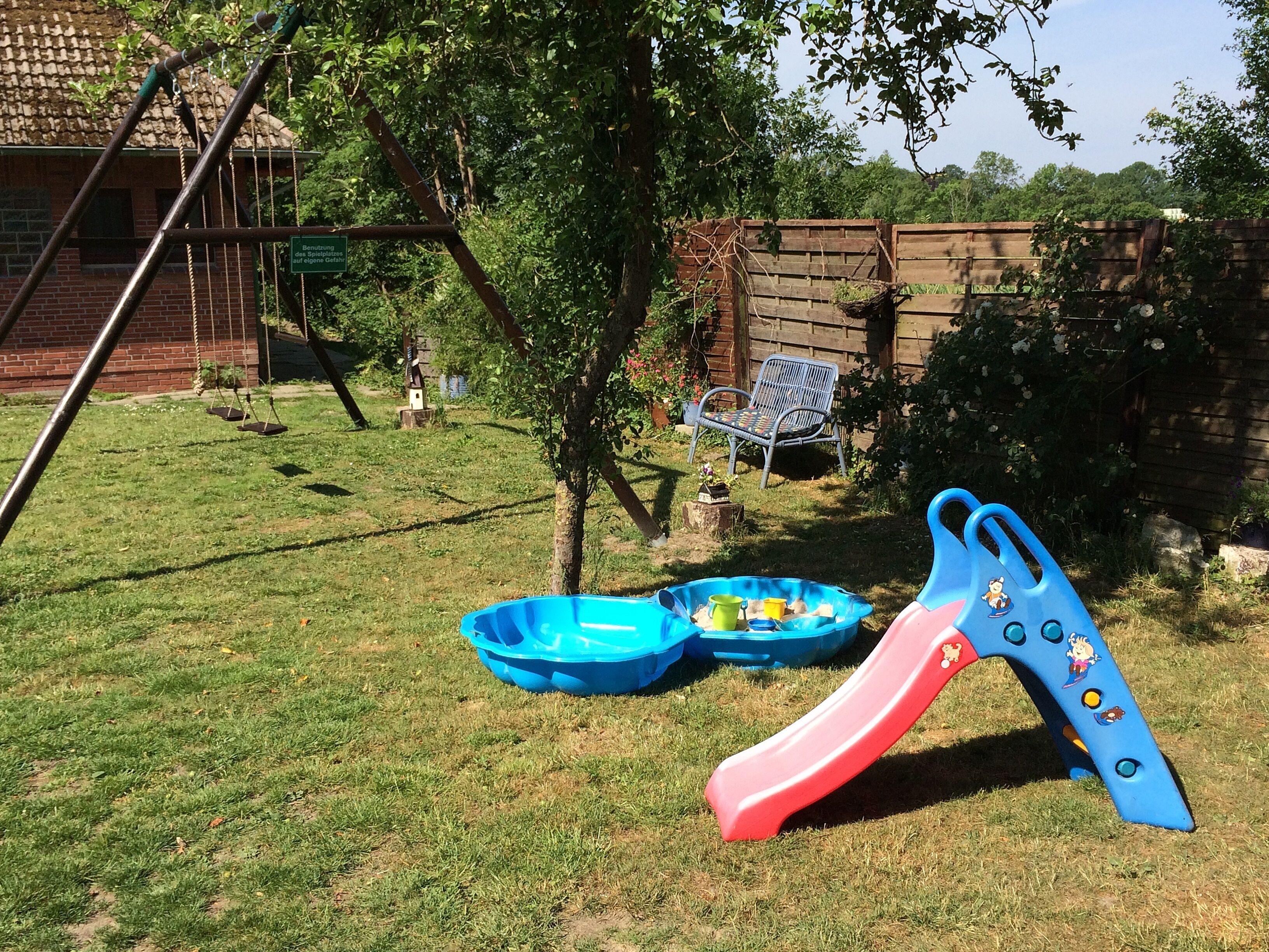 Ein Garten mit Schaukel, Rutsche und einem kleinen blauen Pool mit Spielzeug.
