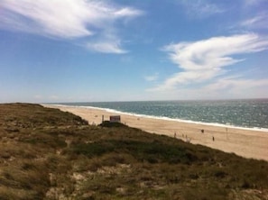 Una playa con cielo despejado y algunas nubes. Se observa una pequeña estructura en la playa, posiblemente un puesto de socorristas.