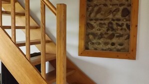 A wooden staircase with a handrail, leading to a lower level. A stone wall with a framed picture is visible on the adjacent wall.