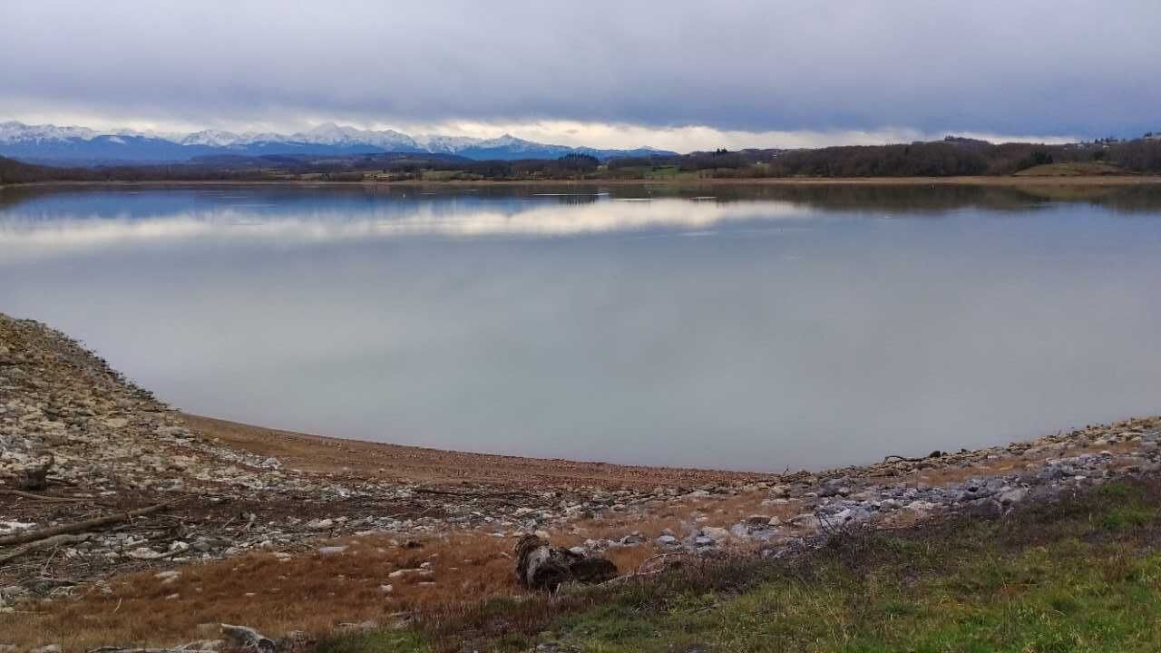 A calm lake with a rocky shoreline and a backdrop of mountains.