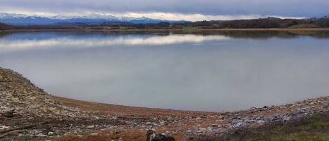 A calm lake with a rocky shoreline and a backdrop of mountains.
