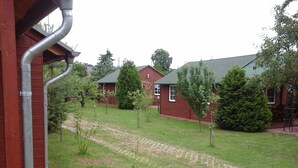 A courtyard with a paved pathway, small trees, and a red building with a grey roof.