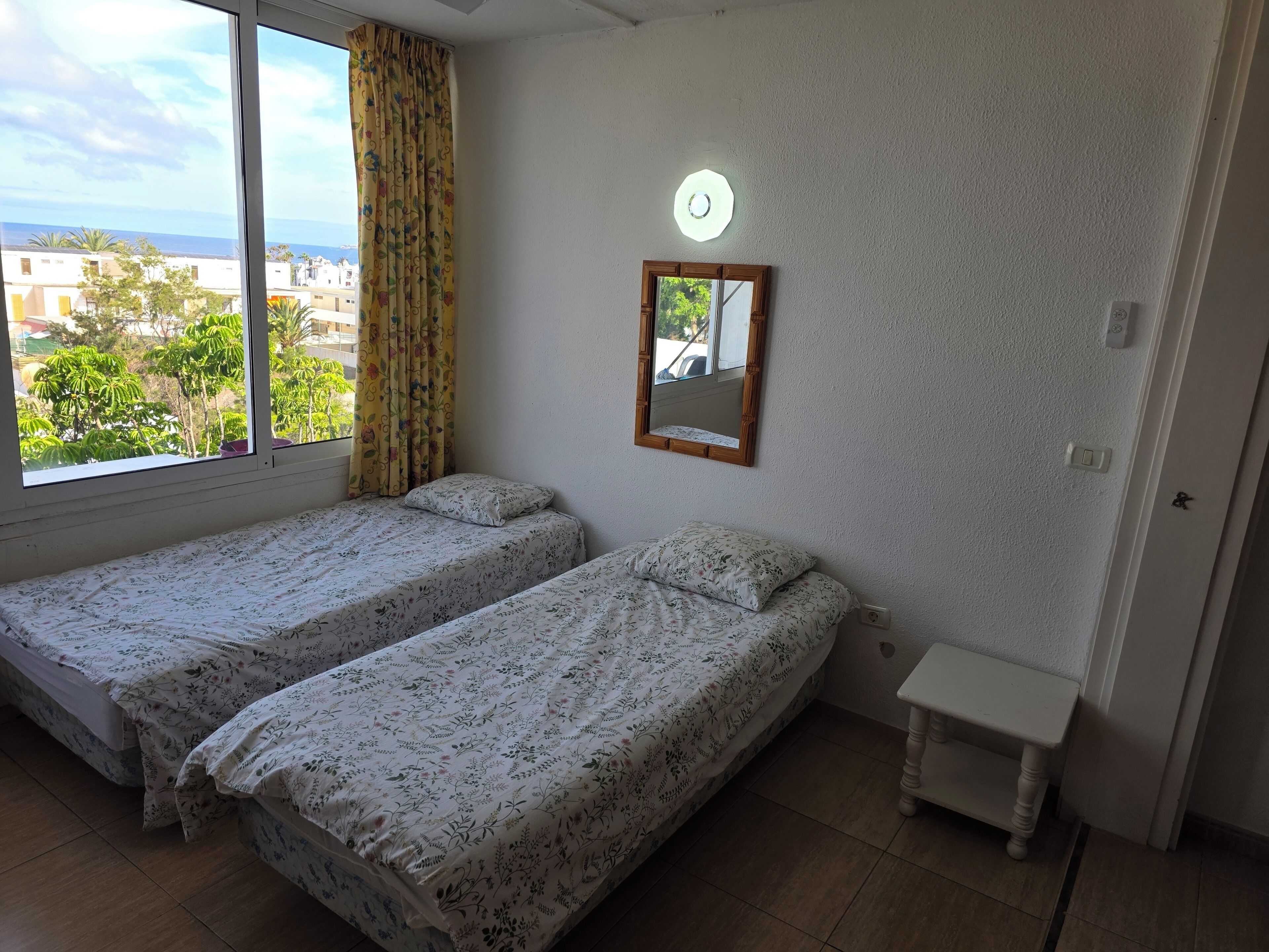 Habitació amb dos llits, una taula petita, un mirall i una finestra amb cortines.