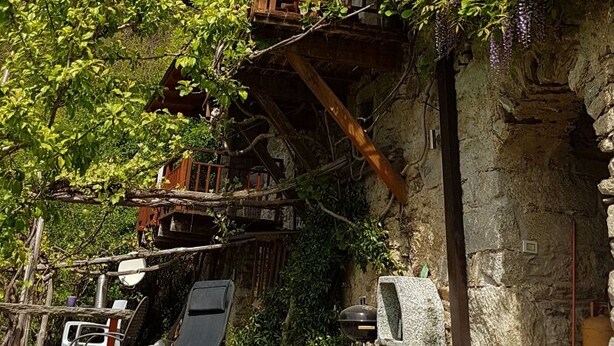 A rustic wooden building with balconies, a stone wall, and outdoor seating.