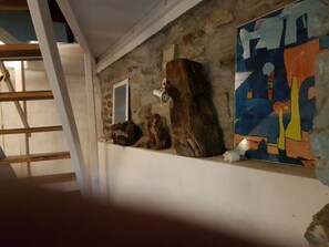 Eine Treppe mit hölzernem Geländer, eine Steinsäule mit rauer Oberfläche und ein Regal mit einem Gemälde und einer kleinen Figur.