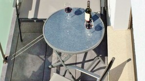 Een klein, rond tafeltje met twee wijnglazen en een fles op een balkon.