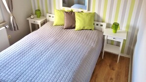 Een opgemaakt bed met een gewatteerde hoes, een nachtkastje met een groen glas erop, en een spiegel erboven.