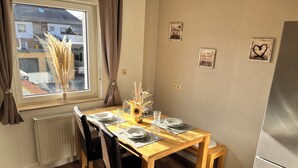 Een eetgedeelte met een houten tafel, zwarte stoelen, een vaas met gedroogde planten en lijstjes met foto's aan de muur.