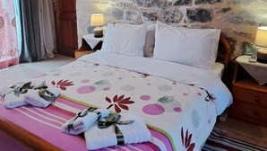 Een slaapkamer met een stenen muur, een bed met een bloemenbedekking, een houten hoofdbord en een nachtkastje met een lamp.