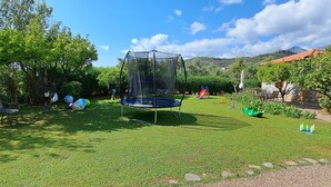 Een achtertuin met een trampoline, stoelen en een speelruimte.
