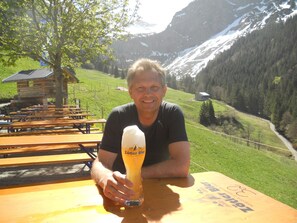 A man sitting at a wooden table outdoors with a beer glass in front of him.