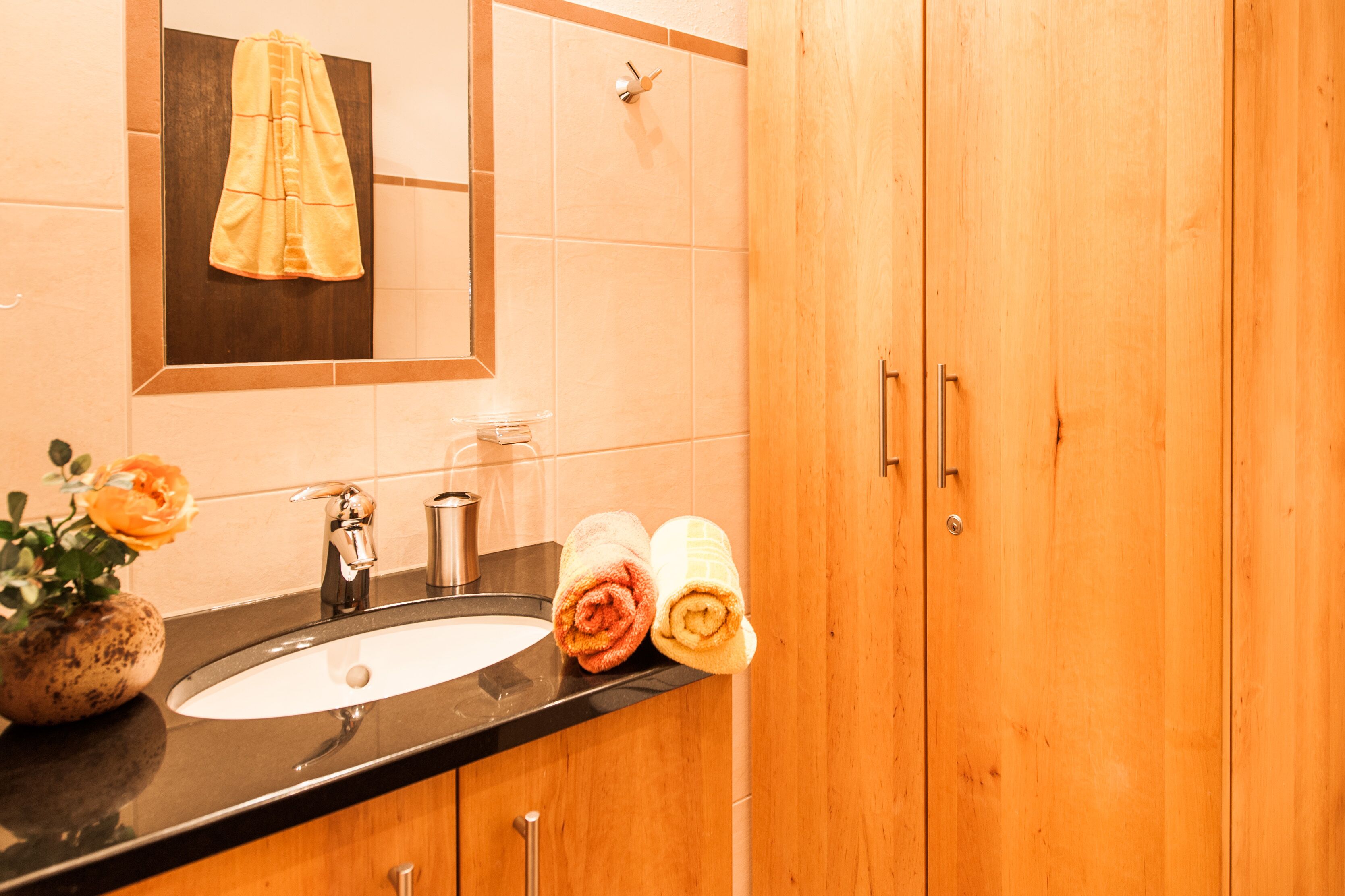 A bathroom with a sink, mirror, wooden cabinets, and two rolled towels.