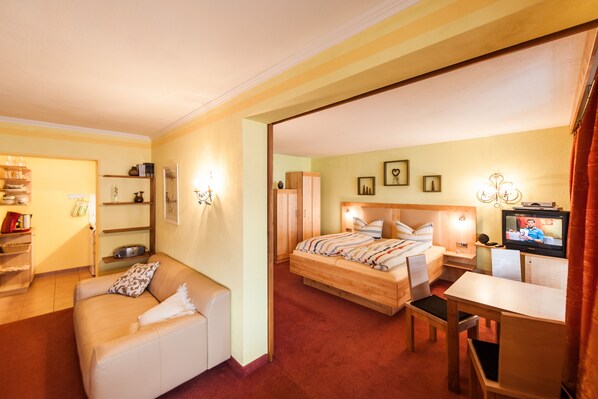 A hotel room with a bed, a desk, a chair, a sofa, and a TV.