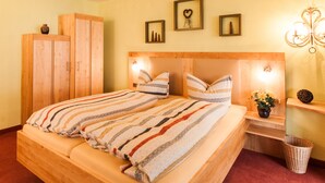 Een houten bed met gestreept beddengoed, een houten kledingkast en een nachtkastje met een bloevas.