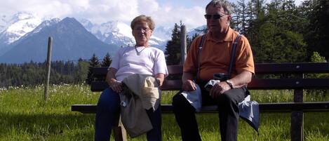Zwei Personen sitzen auf einer Bank, im Hintergrund eine Berglandschaft.