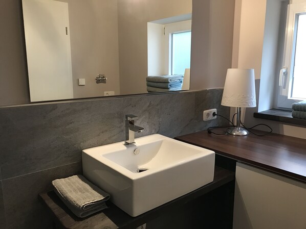 A modern bathroom with a white sink, dark marble backsplash, and a mirror above it.