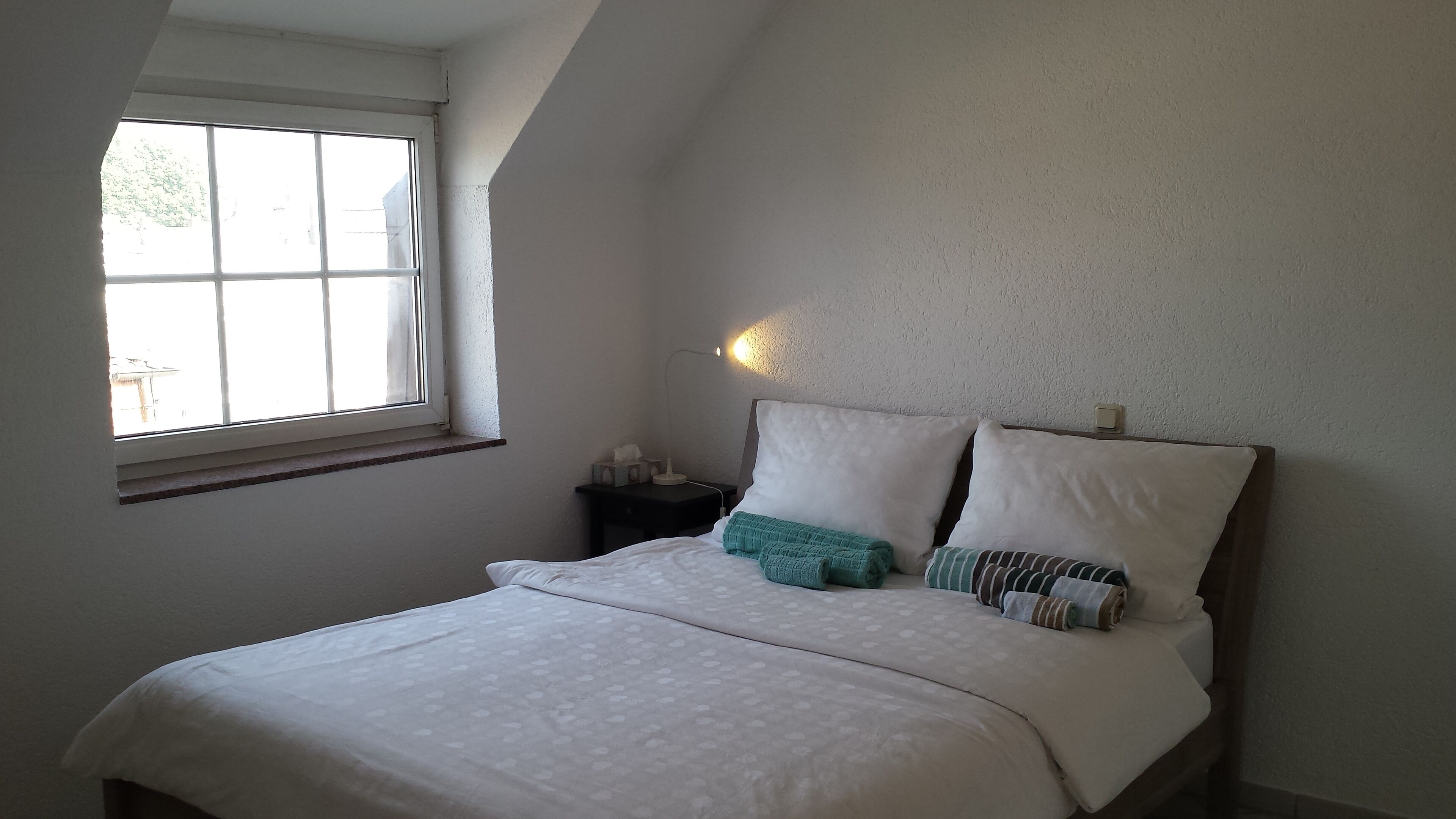 A bedroom with a bed, a nightstand, a lamp, and a window.