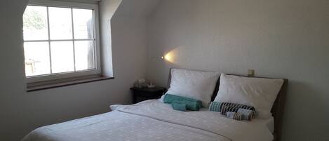 A bedroom with a bed, a nightstand, a lamp, and a window.