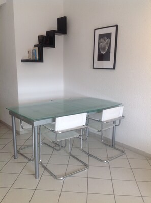 Ein modernes Zimmer mit einem Glastisch und zwei weißen Stühlen, einer Treppe mit schwarzen Stufen und einem gerahmten Bild an der Wand.