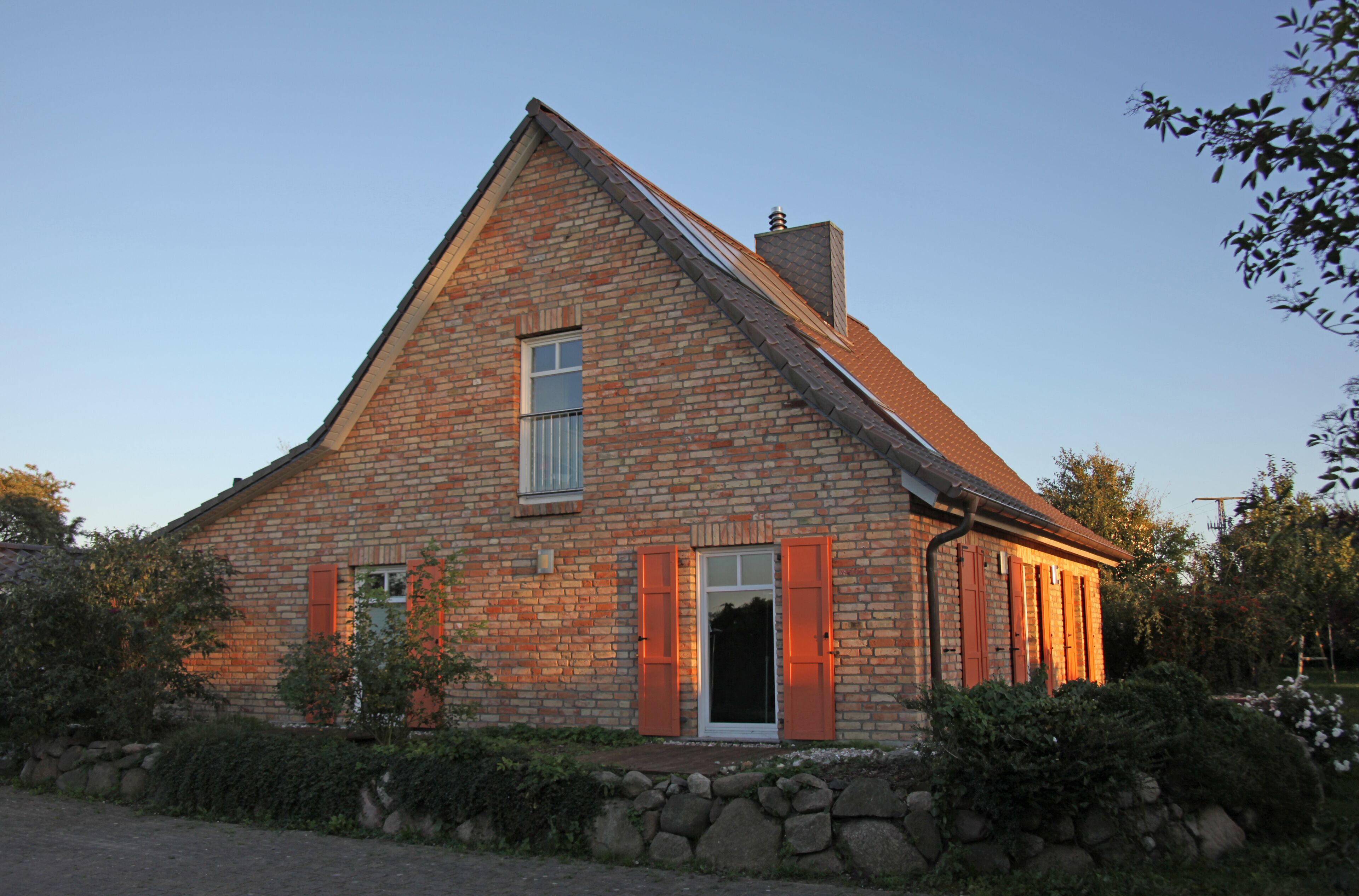 A brick house with a steep gable roof, a chimney, and a small window.