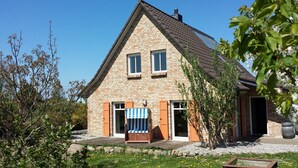 A stone house with a gabled roof, a wooden deck, and a garden with flowers and shrubs. - A lot of space and rest between beach and nature (Sagard)