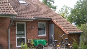 Ein Backsteinhaus mit Ziegeldach und überdachter Terrasse, davor sind zwei Fahrräder abgestellt.
