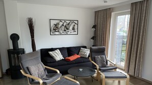Ein modernes Wohnzimmer mit einer schwarzen Couch, zwei Sesseln, einem kleinen runden Tisch und einem Kamin.
