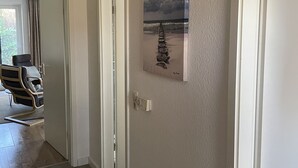 Ein Flur mit einem Gemälde einer Strandansicht, einem Sessel und einer Tür zu einem anderen Raum.